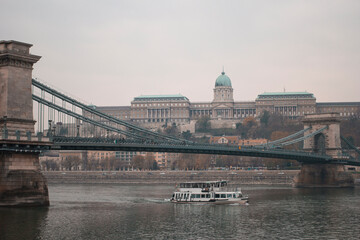 Budapest sunset landscape panorama overlooking the Danube river as a boat passes with the Széchenyi Chain Bridge and the Hungarian National Gallery in the background in Hungary Europe