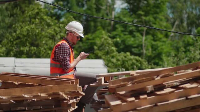 An engineer in a construction uniform talks on the phone against the background of a building under construction