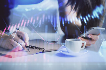 Double exposure of forex graph sketch hologram and woman holding and using a mobile device. Stock market concept.