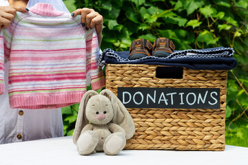 Hands putting a kids sweater in a box for donations on a greenery background. Charity and donation...
