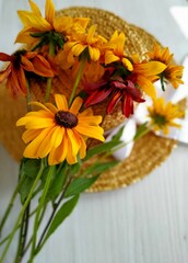 golden bicolor rudbeckia lies on a wicker straw hat on a light wood background. Selective focus