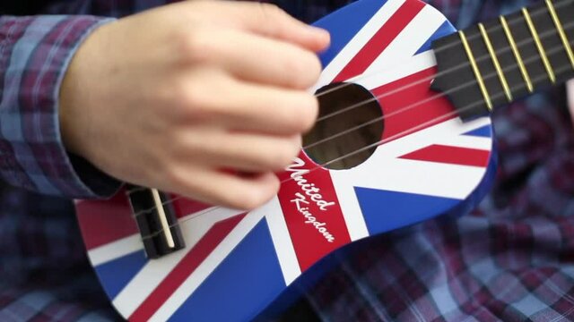 man playing arpeggio and rhythm on ukulele guitar in close up and blurry background. There is a British flag on the ukule.