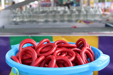 Closeup of red rings in blue bucket for ring toss at carnival, with clear glass bottles in bokeh...
