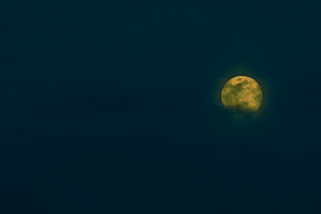 Bright yellow full moon behind clouds