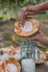 hand get the coconut meat with a spoon from the sliced coconut