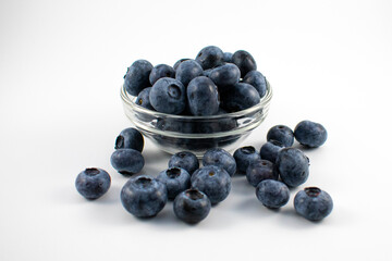 Close up photo of blueberries spilling out of a small glass bowl on a white background