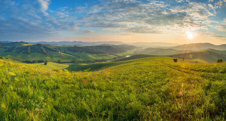 Scenic summer view. Setting sun, beautiful sky. Green hills and meadows.
