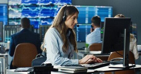 Portrait of female trader or broker working at stock exchange office using headset and computer on background of his business team. Investment Entrepreneur Trading Concept.