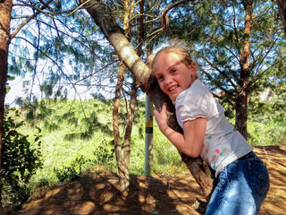 hermosa niña con cabello rubio jugando en los arboles de pino