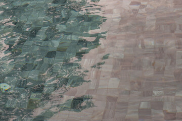 Sun reflection on the blue clear water ripples of swimming pool with mosaic bottom from above. Blue and bright water surface. Copy space, No focus, specifically