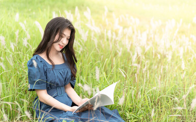 Long-haired girl sitting in the grass, concentrated on reading