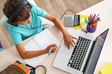 little boy using laptop and headphones studying math during his online lesson