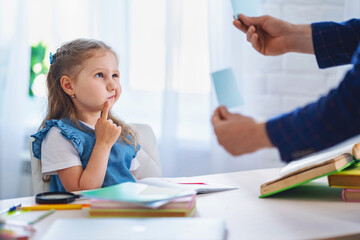little girl thinks about answer in task. child is taught at home with a tutor