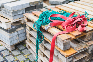 Euro Paletten auf Holz mit roten Spanngurten und einem Grünen Netz auf einer Baustelle