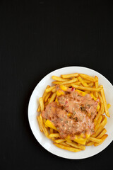 Homemade Animal Style French Fries on a white plate on a black background, top view. Flat lay, overhead, from above. Copy space.