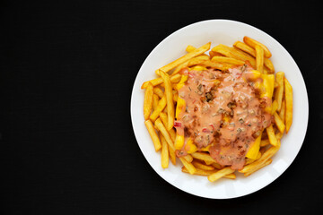Homemade Animal Style French Fries on a white plate on a black background, top view. Flat lay, overhead, from above. Space for text.