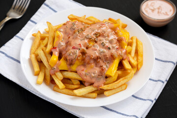 Homemade Animal Style French Fries on a white plate on a black background, side view.