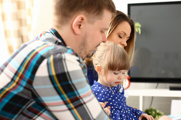 Happy parents with daughter at sofa at home. Beautiful smiling woman and handsome man play with cute little girl childhood and parenthood concept