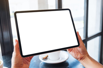 Mockup image of a woman holding black tablet pc with blank white screen with coffee cup on the table