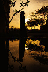 reflection of a young woman wearing a hijab  standing near a water body at dusk DONE!!!