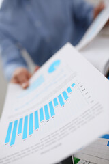 Male hands hold documents with financial statistics at office workspace closeup. White collar check...