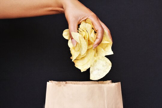 Woman Hand Picking Potato Chips From Brown Paper Bag. Photo Isolate On Black Side View Copy Space