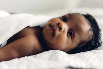 Fototapeta na wymiar Portrait of cute adorable little african american baby looking at camara in a white bedroom