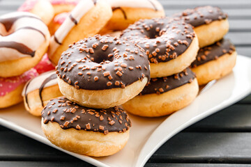 brown chocolate glaze donuts with brown  sprinkles on a white plate on a wooden dark table in a soft light condition, typical american unhealthy fast food
