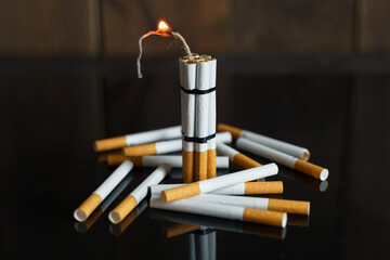 Cigarettes, in the form of sticks of dynamite with a burning wick, stand among the scattered cigarettes on a black reflective surface.