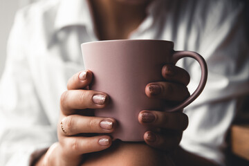 Woman in a white t-shirt holds morning coffee in a pink ceramic cup. Manicure. Front view