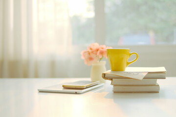 yellow coffee cup sits on top of a book with a spoon on it, on a white table, cup of tea on the table