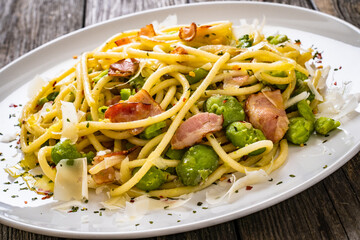 Spaghetti with broad bean, bacon and parmesan on wooden table

