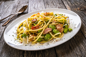 Spaghetti with broad bean, bacon and parmesan on wooden table
