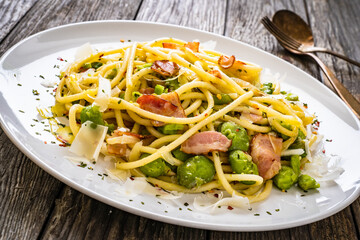 Spaghetti with broad bean, bacon and parmesan on wooden table
