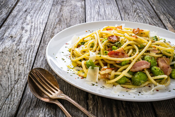 Spaghetti with broad bean, bacon and parmesan on wooden table
