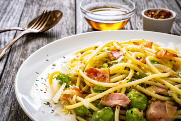 Spaghetti with broad bean, bacon and parmesan on wooden table
