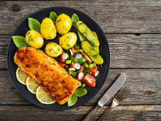 Fish dish - fried breaded cod fillet with vegetables on wooden table
