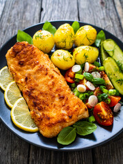Fish dish - fried breaded cod fillet with vegetables on wooden table
