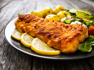 Fish dish - fried breaded cod fillet with vegetables on wooden table
