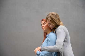 Two happy girlfriends are hugging on the background of a gray wall. Gentle hugs of a female lesbian couple. LGBT Same-sex marriage.