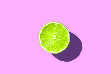 half sliced green fresh lime with hard shadow on purple or pink background isolated. green lime summer concept