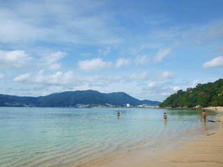 Fototapeta na wymiar Tropical island in Thailand. People, swimming in the sea. Popular resort. Beach on Phuket. Thai paradise. Beautiful sky with cumulus clouds. Palm trees, green hills, a beautiful bay. Azure clear water
