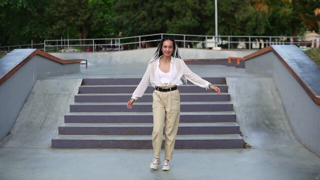 Funny dancing girl in the street or park in front the stairs. Cheerful and happy young woman dancing while walking along the street, looking over shoulder. She's wearing a white blouse and beige pants