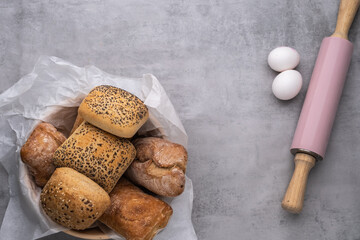 Mixed bread in basket with egg and rolling on dark background.