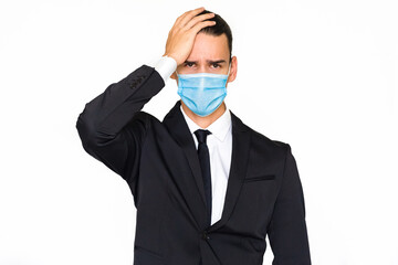 Worried businessman stressed with hand on face wearing a blue face mask and a suit. Isolated against a white background. 
