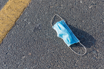 Used disposable medical face mask left discarded on the road in the city. Environmental pollution and waste during the Covid-19 pandemic.