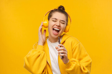 Trendy girl singing favorite song out loud in phone as mic, wearing wireless headphones, isolated...