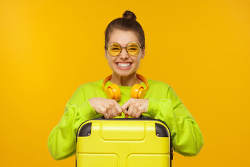 Happy excited girl holding travel suitcase ready for summer trip, isolated on yellow background