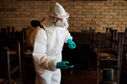 Sanitation worker in protective suit disinfecting empty cafe during coronavirus epidemic.