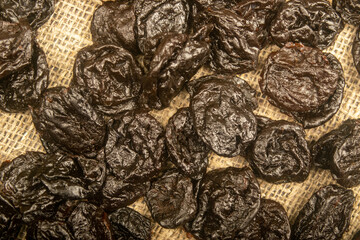 Dried prunes in bulk on burlap with a rough texture. Close up.